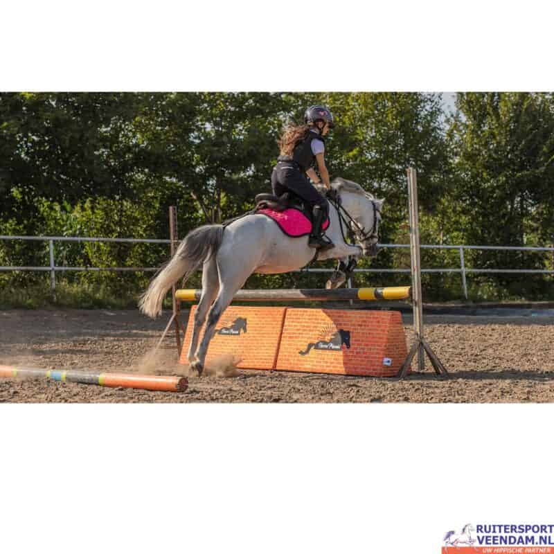 Jonge ruiter springt over foam muur met haar paard tijdens training.